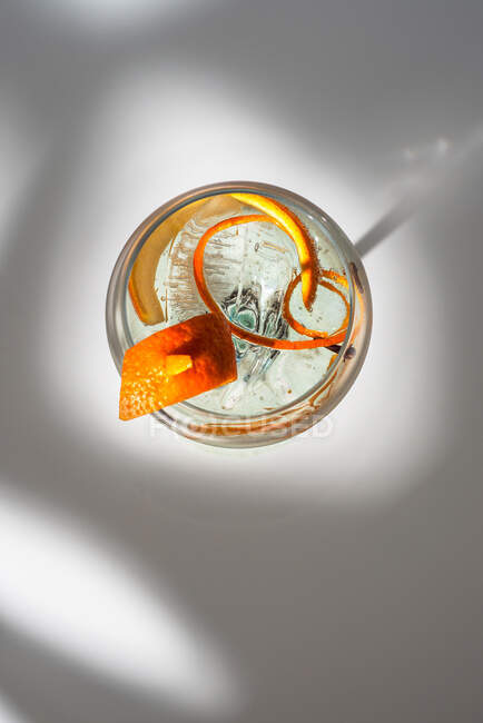 Vista dall'alto di vetro trasparente di cocktail highball decorato con scorza di agrumi e chiodi di garofano contro le ombre alla luce del sole — Foto stock