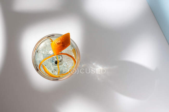 Top view of transparent glass of highball cocktail decorated with citrus fruit zest and clove against shadows in sunlight — Stock Photo
