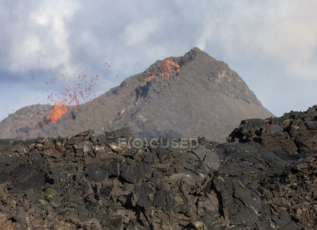 Vista lateral de las chispas de magma fuera del agujero del volcán y correr como ríos de lava sobre el suelo en Islandia - foto de stock