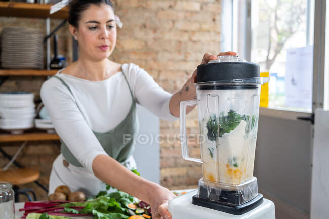 Foglie di bietola miscelazione femminile con latte vegetariano in elettrodomestico da cucina durante la preparazione di bevande sane in casa — Foto stock