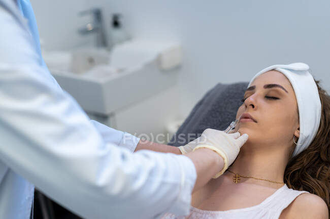 Зверху невпізнаваний професійний косметолог зі шприцом, який впорскує філер з гіалуроновою кислотою в губах клієнтів під час процедури в клініці краси. — Stock Photo