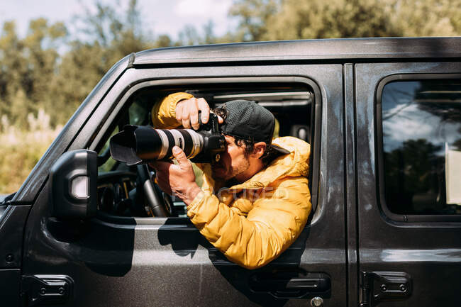 Seitenansicht eines abenteuerlustigen Fotografen, der Fotos aus dem Inneren seines Geländewagens macht — Stockfoto