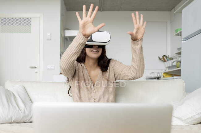 Unrecognizable cheerful female with gamepad experiencing virtual reality in goggles while playing video game on couch in house — Stock Photo