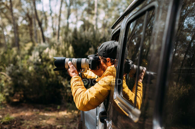 Vista lateral de um fotógrafo aventureiro tirando fotos de dentro de seu carro off-road — Fotografia de Stock
