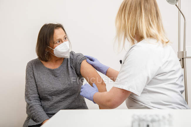 Especialista médica em uniformes de proteção e luvas de látex vacinando a paciente idosa na clínica durante o surto de coronavírus — Fotografia de Stock