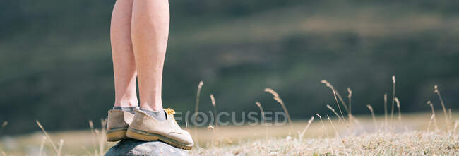 Side view of crop female hiker in boots standing on rock in nature during trekking in summer — Stock Photo