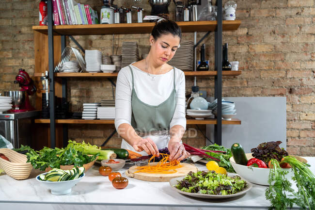 Konzentriertes Weibchen mit roher Karotte bereitet vegetarisches Essen im Haus zu Moderne Küche — Stockfoto