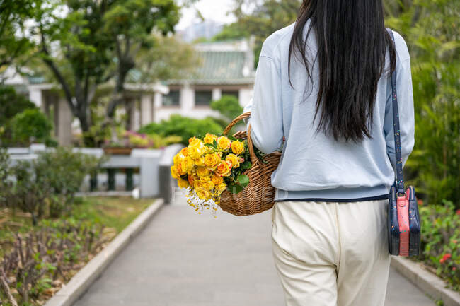 Detail of beautiful Asian's girl in a park while she carries a wicker basket with yellow flowers. — Stock Photo