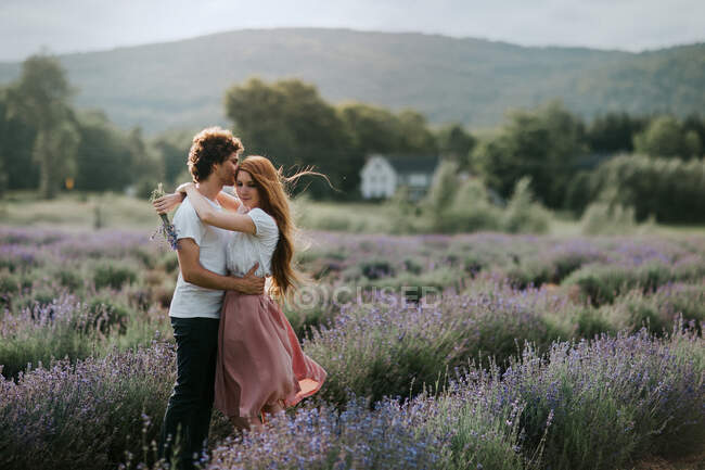 Casal sereno em pé no campo de lavanda com flores florescentes e olhando para longe — Fotografia de Stock