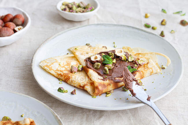 Vista superior de deliciosas crepes adornadas con chocolate y nueces servidas en el plato en la mesa para el desayuno - foto de stock