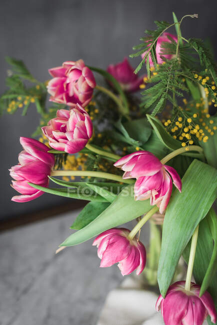 Fleurs roses fleuries avec des pétales doux et des feuilles vertes dans un vase sur fond gris — Photo de stock