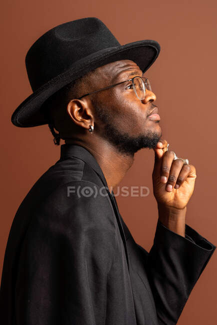 Side view of young masculine unshaven African American male with naked abdomen in jacket looking away on brown background — Stock Photo