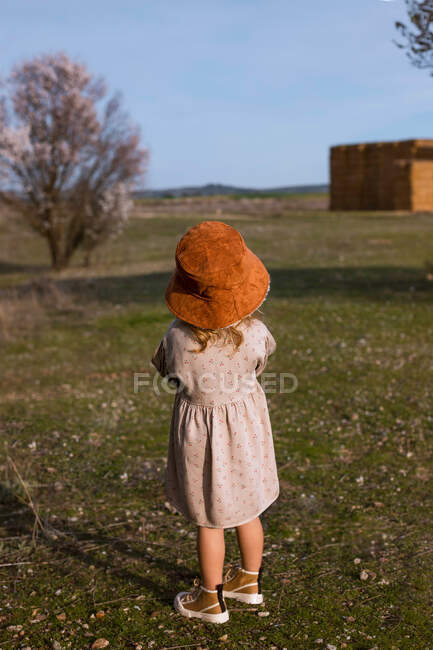Kleines Kind im Kleid steht neben blühendem Baum mit Blumen im Frühlingspark und schaut weg — Stockfoto