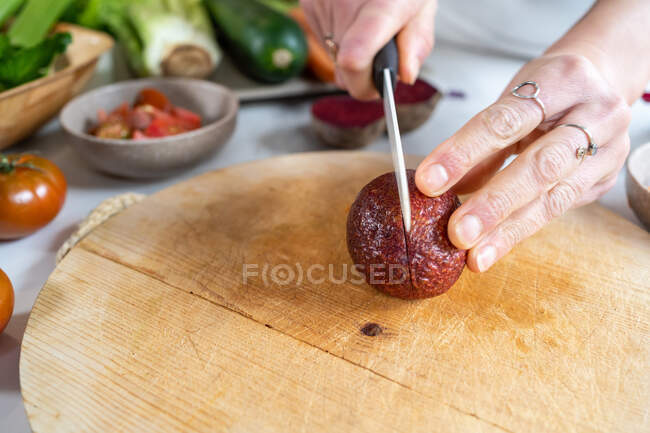 Cultivo femenino anónimo con corte de cuchillo mitades de aguacate maduras por encima de la tabla de cortar durante el proceso de cocción en casa - foto de stock