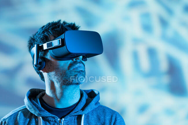 Homme barbu méconnaissable en sweat à capuche et casque moderne explorant la réalité virtuelle sous la lumière du néon — Photo de stock