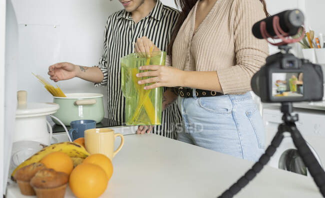 Обрізати невпізнавані відеоблогери готуючи макарони під час запису відео на фотокамеру за столом зі свіжими фруктами — стокове фото