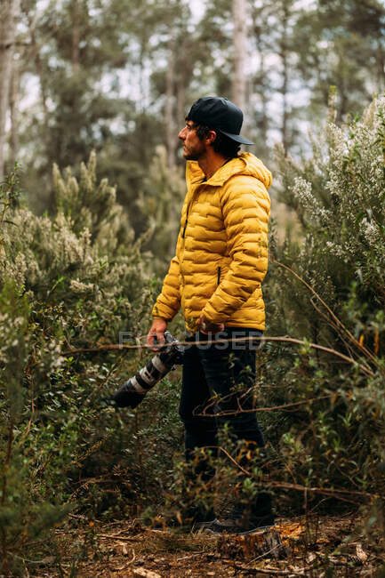 Side view of a photographer in a cap and yellow jacket on the mountain looking away — Stock Photo