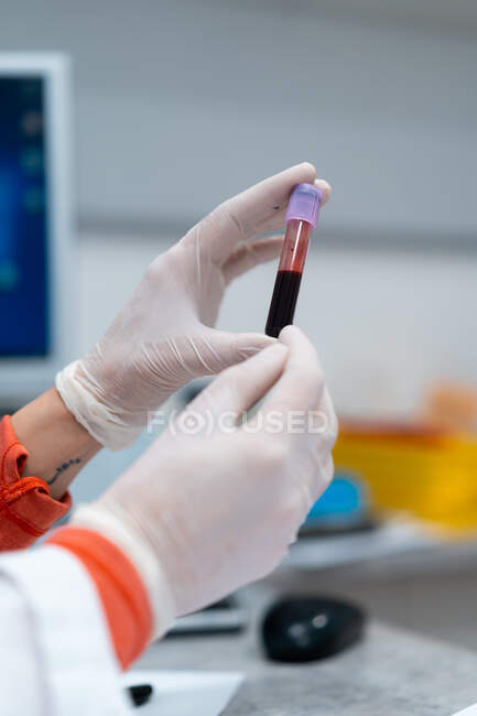 Неузнаваемая женщина-медик в маске и перчатках держит трубку с образцом крови в современной лаборатории в клинике — стоковое фото