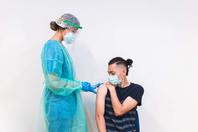 Ärztin in Schutzuniform, Latexhandschuhen und Gesichtsmaske impft hispanischen Mann während Coronavirus-Ausbruch in Klinik — Stockfoto