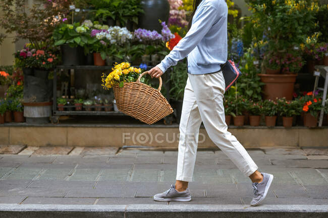 Вид сбоку на тело девочки, несущей корзину с цветами во время прогулки — стоковое фото