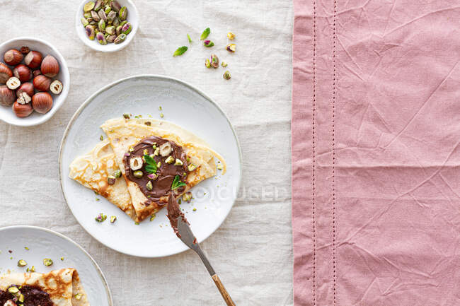 Vista superior de deliciosos crepes decorados com chocolate e nozes servidos na placa na mesa para o café da manhã — Fotografia de Stock