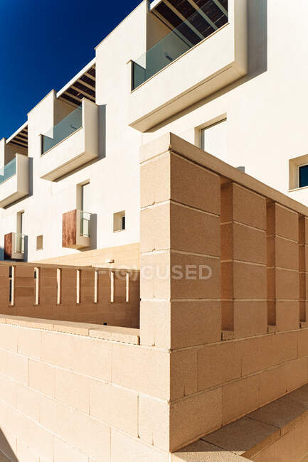 Fachada de casa moderna com parede de alvenaria e pequenas varandas sob o céu azul na cidade à luz do sol — Fotografia de Stock