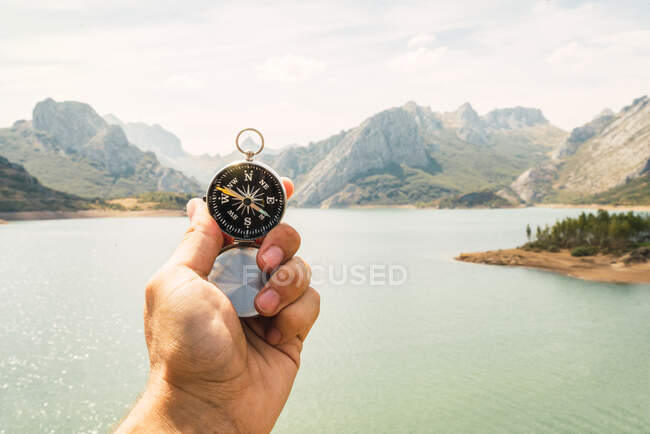 Nahaufnahme einer Hand, die einen Kompass in einer herrlichen Landschaft mit Fluss und Bergen hält — Stockfoto