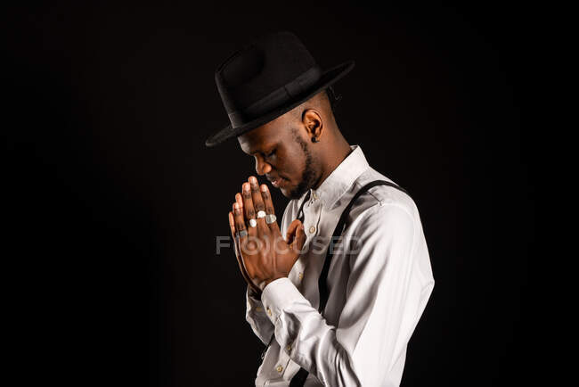 Vista lateral do jovem homem afro-americano sem barba em camisa branca e anéis nos dedos com as mãos de oração — Fotografia de Stock