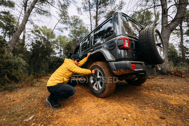 Vista lateral de um aventureiro verificando a pressão das rodas de seu carro off-road nas montanhas — Fotografia de Stock