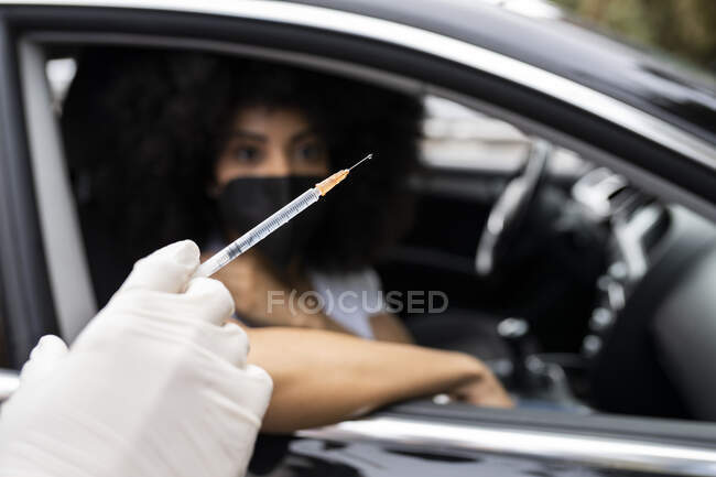 Cropped unrecognizable nurse in latex gloves and uniform vaccinating African American female patient inside the car on a drive through mobile clinic during coronavirus outbreak — Stock Photo