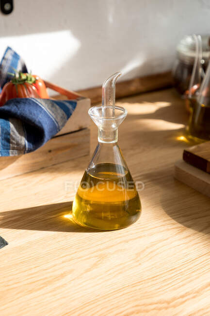 Tarro de vidrio con aceite de oliva aromático natural colocado en la mesa de madera en la cocina casera - foto de stock