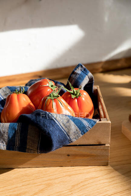 Alto ângulo de tomates vermelhos maduros frescos colocados na bandeja de madeira natural com guardanapo na cozinha doméstica — Fotografia de Stock