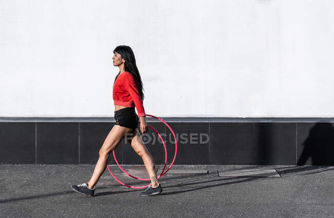 Seitenansicht einer fitten jungen Frau in Sportkleidung mit Reifen, die auf dem Gehweg spaziert, während sie sich im Sonnenlicht nach vorne freut — Stockfoto