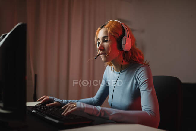 Seitenansicht einer begeisterten Spielerin mit Kopfhörer, die zu Hause am Tisch sitzt und Videospiele spielt — Stockfoto