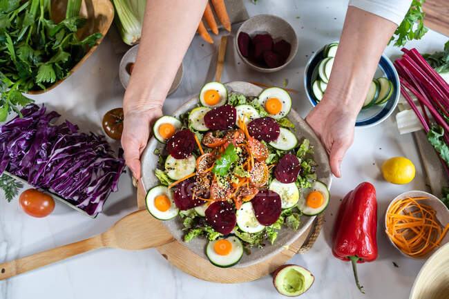 Зверху обрізана невизначена жінка, що демонструє смачний овочевий салат на тарілці за мармуровим столом — стокове фото