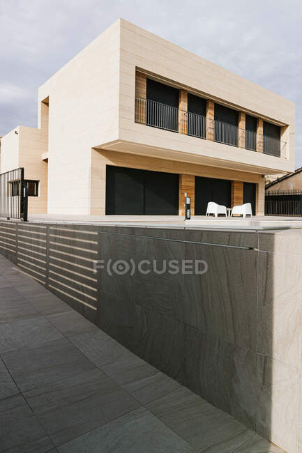 Contemporary masonry building exterior with fenced balcony against mount and walkway under cloudy sky in town — Stock Photo