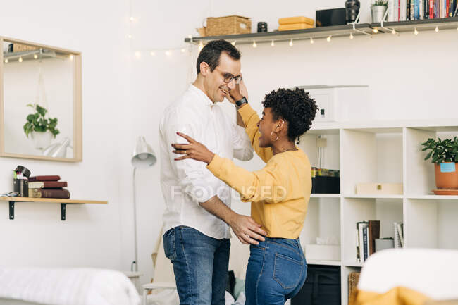 Side view of delighted multiracial couple dancing in living room while spending time together at home — Stock Photo