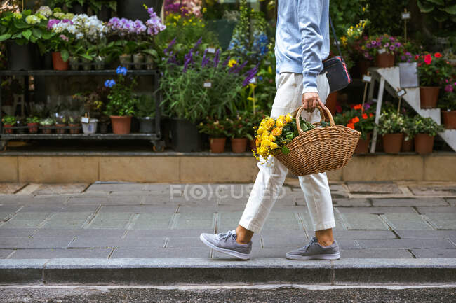 Vista lateral do corpo da menina carregando uma cesta de flores enquanto ela caminha — Fotografia de Stock