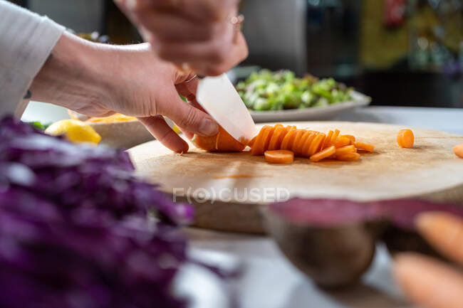 Врожай невизначена жінка, що ріже сиру моркву ножем під час приготування вегетаріанської їжі в будинку — стокове фото