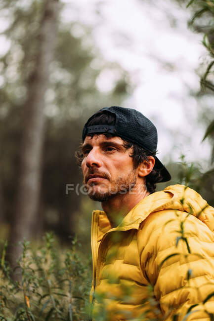 Retrato de un hombre con gorra y chaqueta amarilla mirando hacia la montaña con fondo borroso - foto de stock