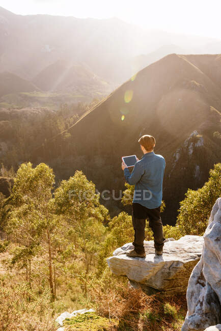 Tranquil male explorer with tablet standing on hill in mountainous terrain at sunset — Stock Photo