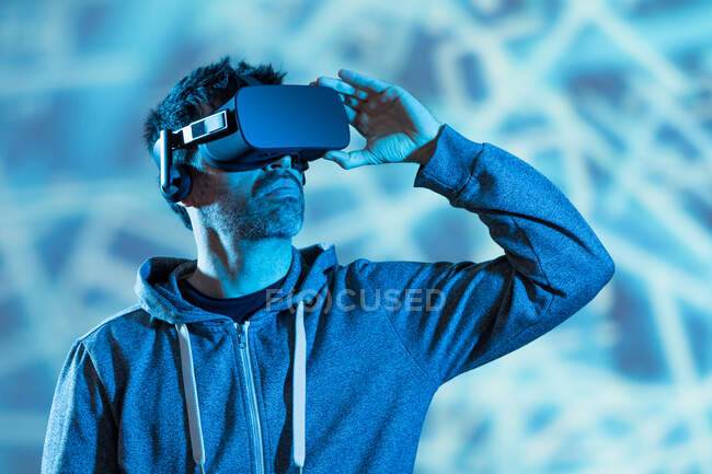 Unerkennbarer bärtiger Mann in Kapuzenpulli und modernem Headset erkundet virtuelle Realität im Neonlicht — Stockfoto