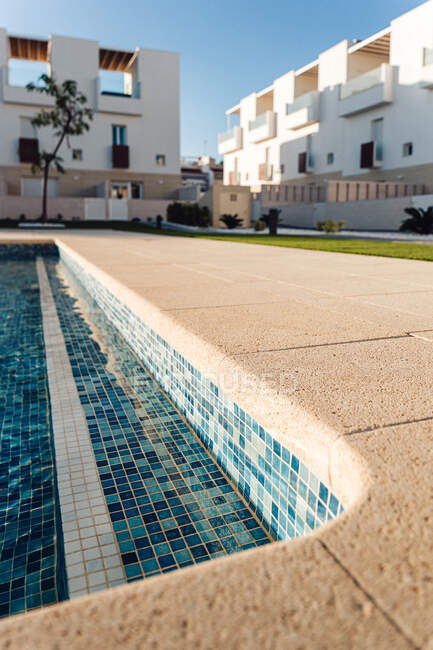 Maison contemporaine extérieurs contre piscine avec eau ondulée et pelouse sous le ciel bleu en ville — Photo de stock
