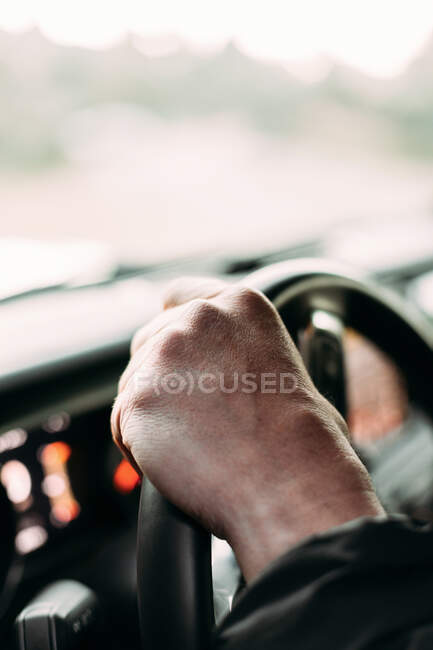 Вид на урожай анонимного человека с рукой на руле автомобиля на фоне размытости — стоковое фото