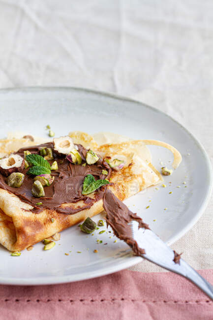 Deliciosas crepas adornadas con chocolate y nueces servidas en el plato en la mesa para el desayuno - foto de stock