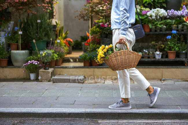 Вид сбоку на тело девочки, несущей корзину с цветами во время прогулки — стоковое фото