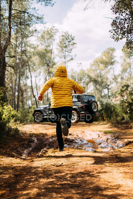 Back view of hooded adventurer running next to his off-road car on the road — Stock Photo