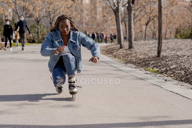 Afro-americano pattinaggio femminile lungo la strada nella giornata di sole in estate e godersi il fine settimana in città — Foto stock
