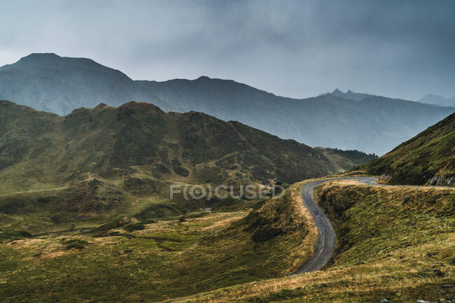 Paysage pittoresque de route vide entouré d'herbe sèche et verte en terrain montagneux de la vallée d'Aran en Espagne sous un ciel gris nuageux — Photo de stock