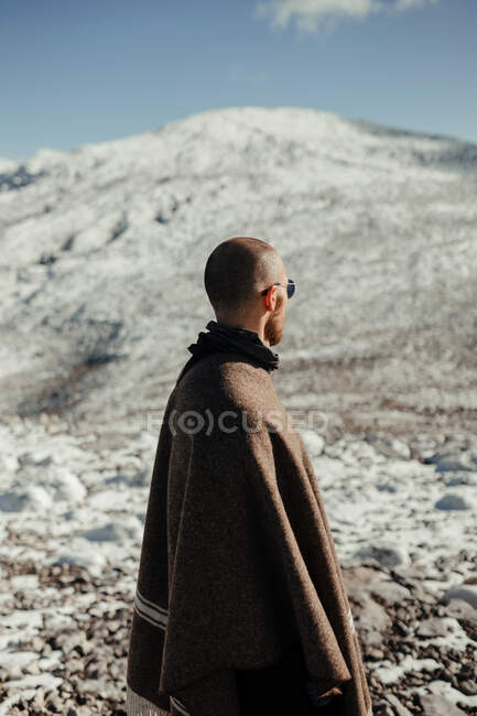 Турист на мысе с видом на снежную гору под голубым облачным небом зимой — стоковое фото